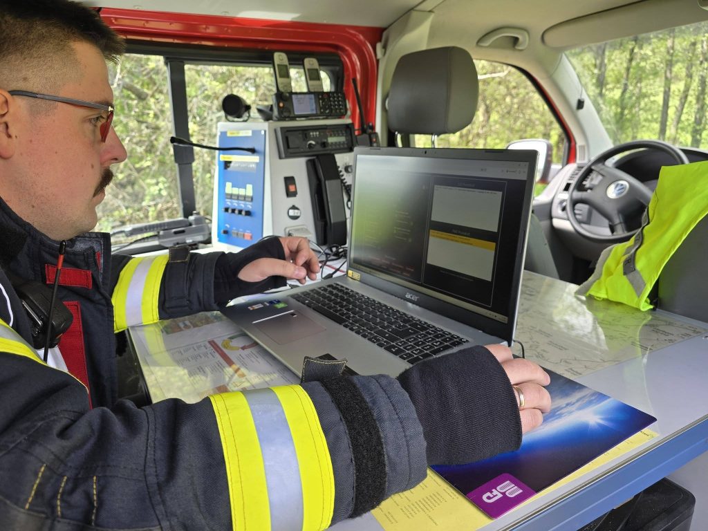 Niklas Hartmann in Feuerwehr-Uniform bei einem Einsatz als Einsatzleiter vor einem Laptop.