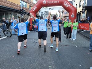 Mitarbeiter (von hinten fotografiert) laufen jubelnd ins Ziel beim Firmenlauf 2026 in Bad Marienberg